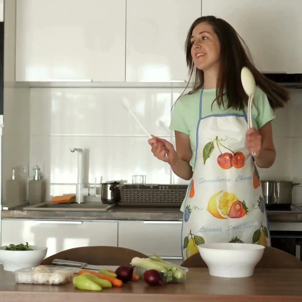 A woman happily playing the drums with her spatula in the kitchen.