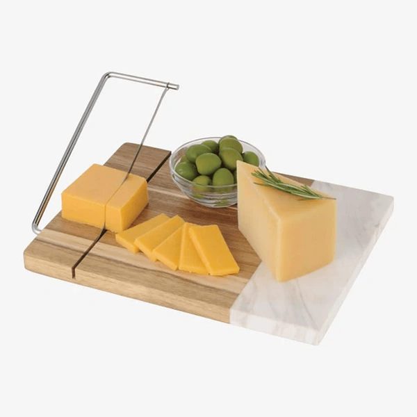 Cheese slicer with various cheeses and olives on a wooden and marble board.