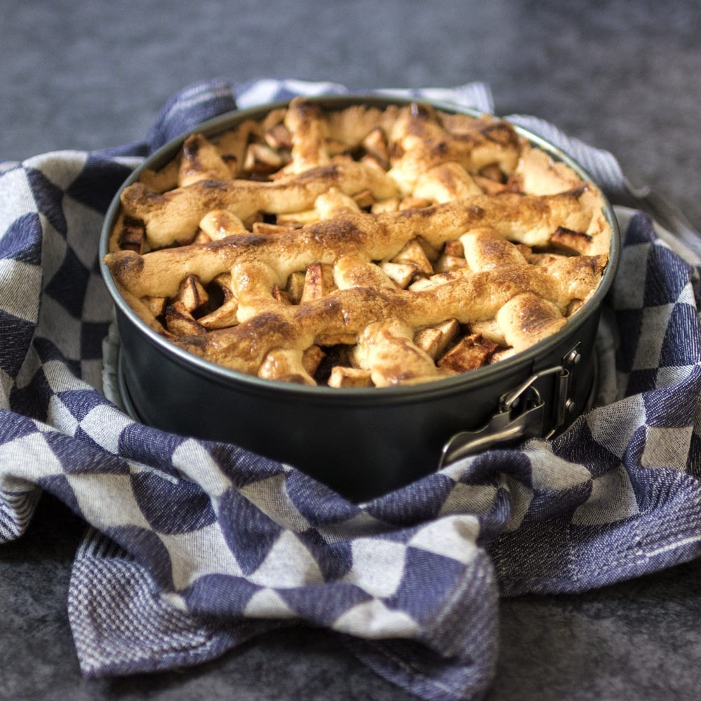 Homemade apple pie in a black baking dish on a blue checkered cloth