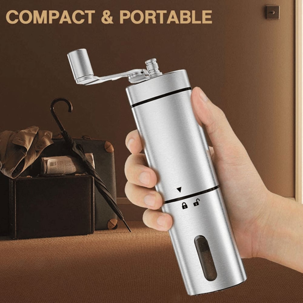 Hand holding a compact and portable stainless steel manual coffee grinder with suitcase and umbrella in the background.