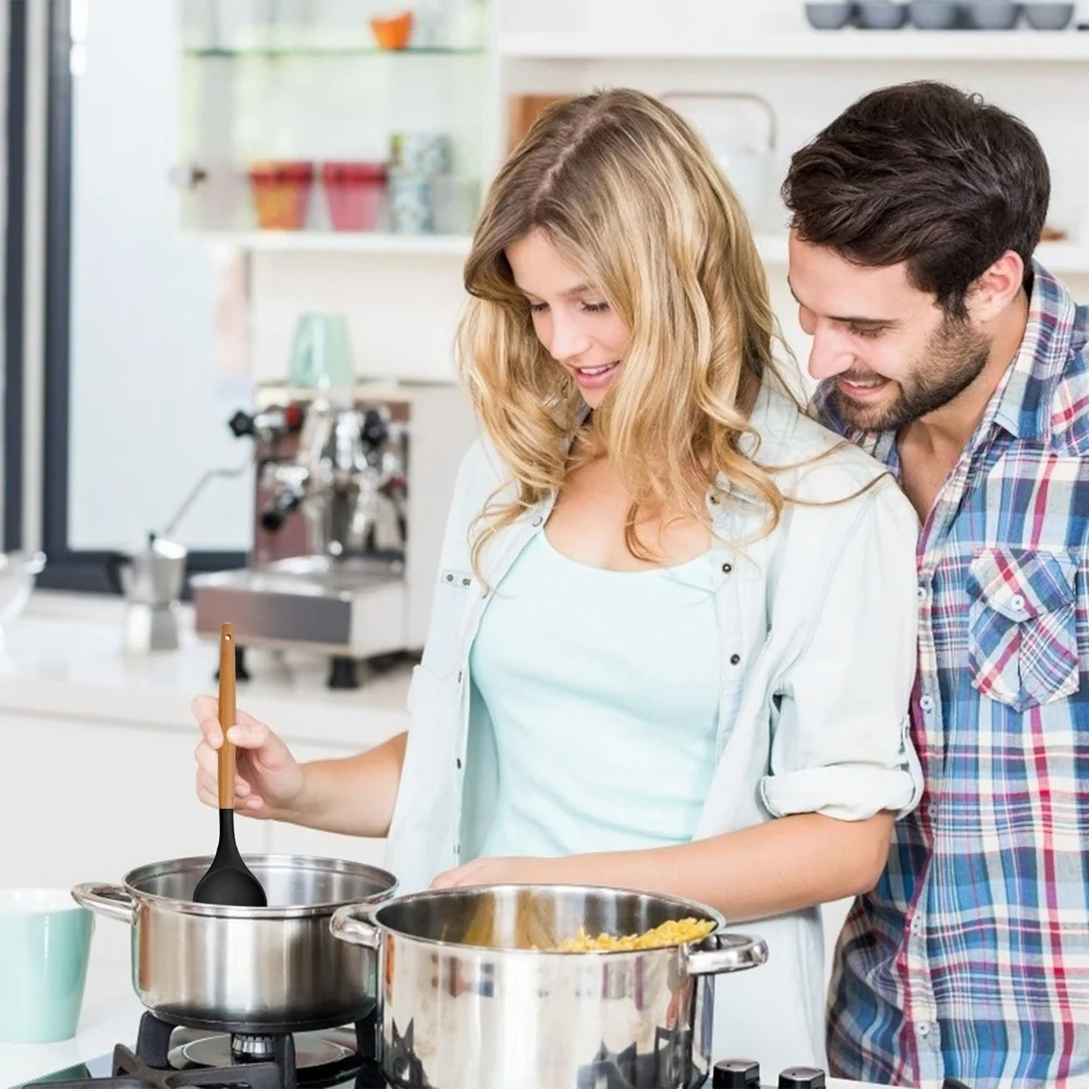 Couple cooking together in a modern kitchen holding a ladle over a pot on the stove.