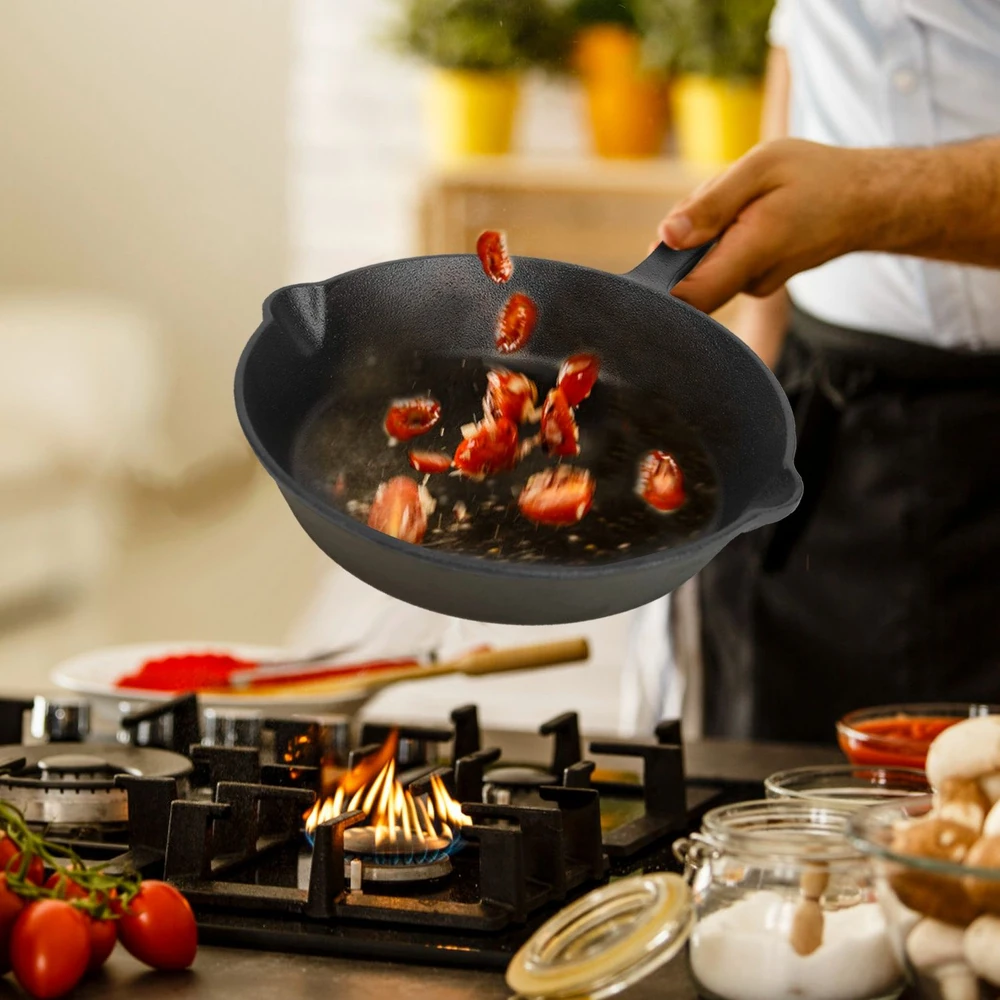 Chef tossing cherry tomatoes in a black skillet over a gas stove in a kitchen.
