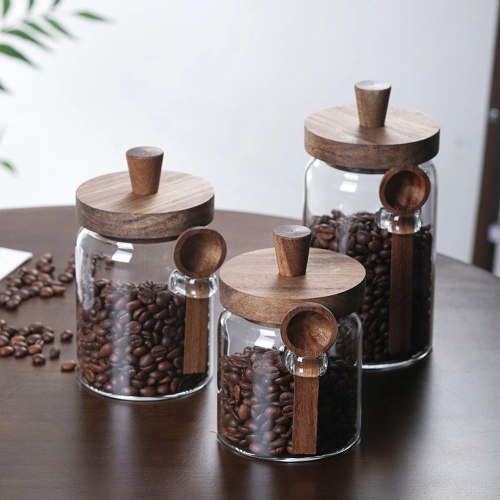 Three glass jars filled with coffee beans, each with a wooden lid and spoon.