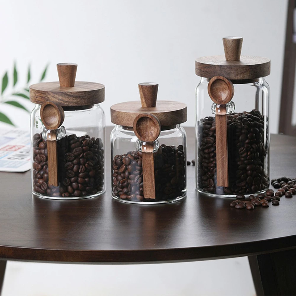 Three glass jars with wooden lids and scoops filled with coffee beans on a wooden table.
