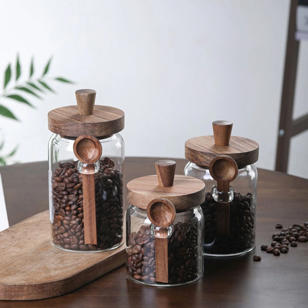 Wooden-lidded glass jars filled with coffee beans on a wooden table, each jar featuring a matching wooden scoop attached to the lid.