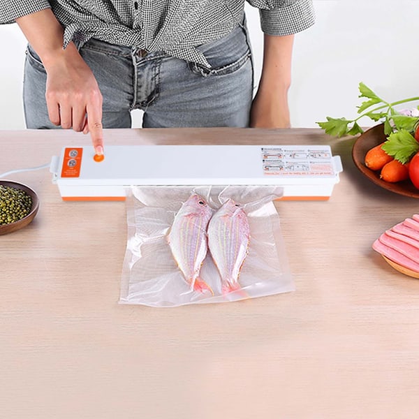 Person using a vacuum sealer to seal fish on a kitchen countertop with vegetables nearby.