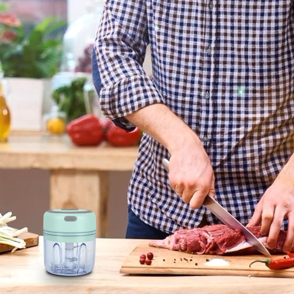 Man cutting raw meat on a wooden chopping board in a kitchen with a small electric food chopper placed nearby.